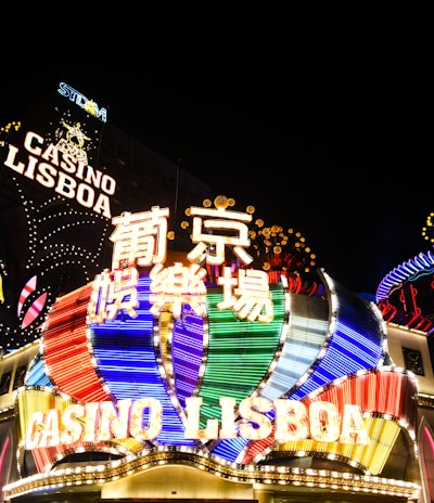 Bright neon signs in multiple colors illuminate the night, prominently displaying the name 'Casino Lisboa' alongside signage in Chinese characters. The lights form intricate patterns and vibrant displays, creating a lively and energetic atmosphere.